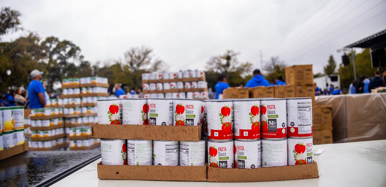 Volunteers at a community food drive organizing canned goods for distribution outdoors.