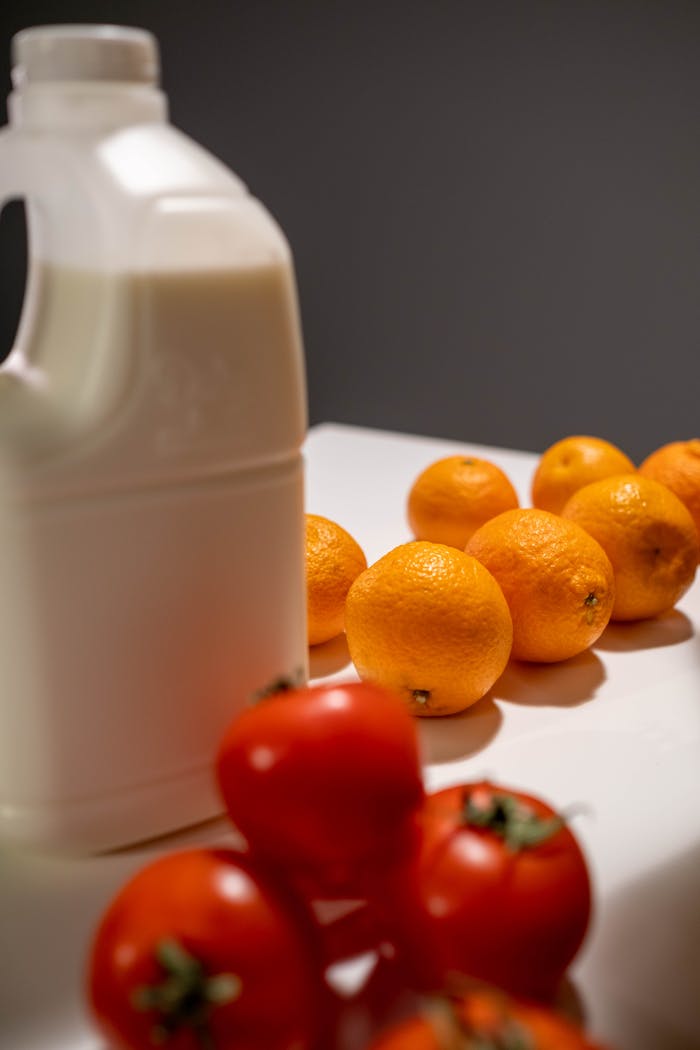 A still life composition featuring tomatoes, oranges, and a milk bottle.